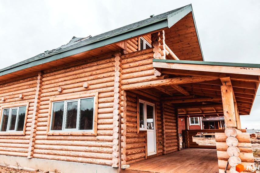 Котеджне містечко КМ Святобор: дерев'яний будинок з верандою та вікнами, що виходять у ліс. Навколо будинку - будівельний майданчик.