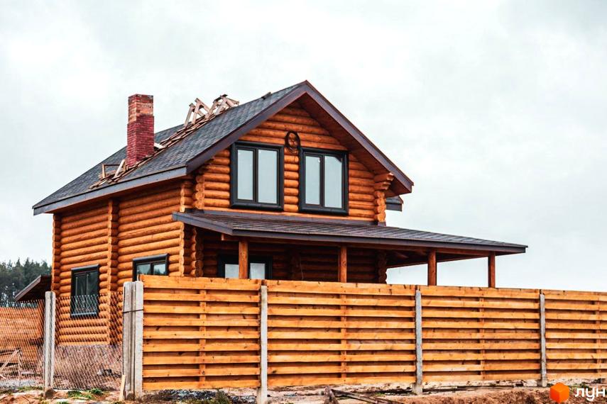 Котеджне містечко Святобор: двоповерховий дерев'яний будинок з цегляним димарем та огорожею з дерев'яних дощок. Навколо будинку видно елементи будівництва та паркан.