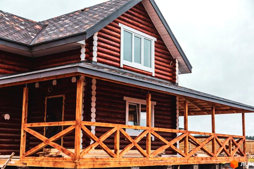 Котеджне містечко Святобор: двоповерховий будинок з бруса з великою терасою та дерев'яними перилами. Навколо будинку видно елементи прибудинкової території.