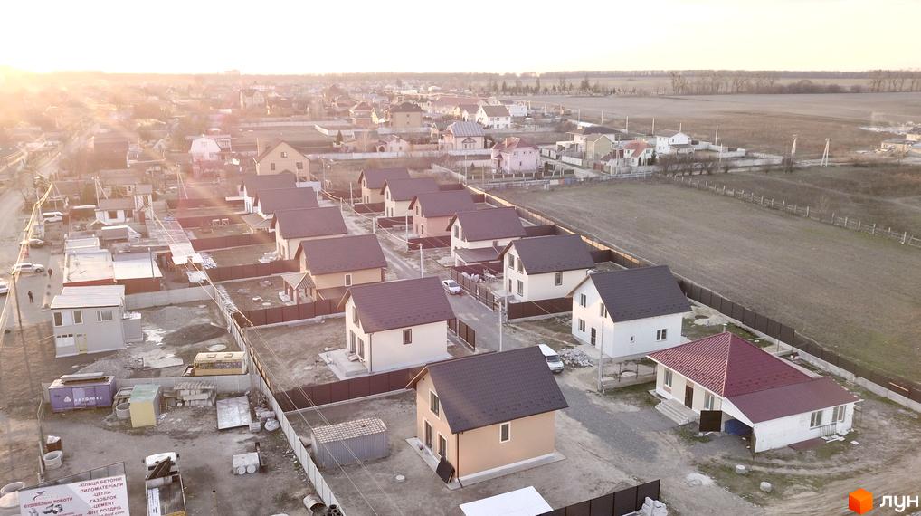 Котеджне містечко КМ Green House: сучасні будинки з коричневими дахами та доглянутою прибудинковою територією. Забудова розташована біля поля під яскравим сонцем.