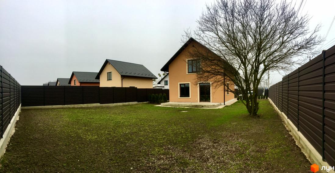 Котеджне містечко КМ Green House. Одноповерхові будинки з темним дахом та світлими стінами, огороджені темним парканом. На території зелений газон та дерева.
