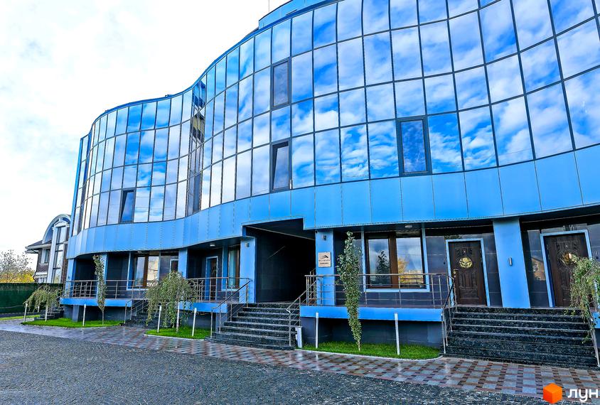 Фасад житлового комплексу Sky River з панорамним склінням та блакитним оздобленням. Перед будинком розташовані сходи, доріжки та зелені насадження.