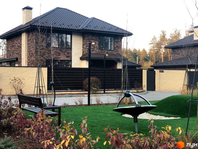 Котеджне містечко КМ Zahrava Village: двоповерхові будинки з коричневою черепицею та цегляним фасадом, зелений двір з дитячим майданчиком та лавкою.