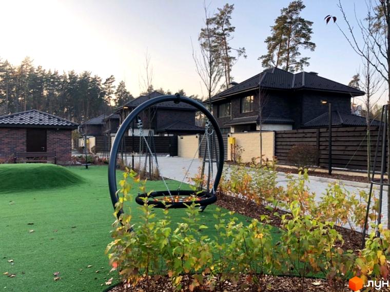 Котеджне містечко Zahrava Village. Чорні дахи будинків, зелений газон та дитячий майданчик з гойдалкою.