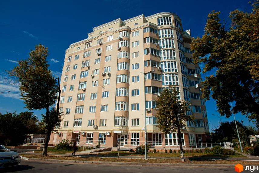 Новобудова на вулиці Михайла Драй-Хмари, 44, з багатоповерховими секціями та вигнутим фасадом. Навколо будівлі розташовані дерева та міська інфраструктура.