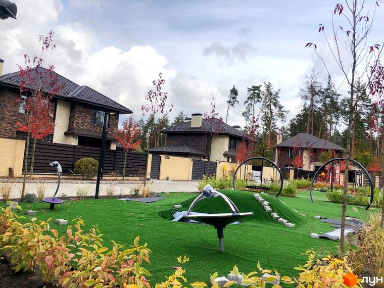 Котеджне містечко Zahrava Village: двоповерхові будинки з коричневими дахами та цегляними фасадами. На території дитячий майданчик з яскравим покриттям та елементами для гри.