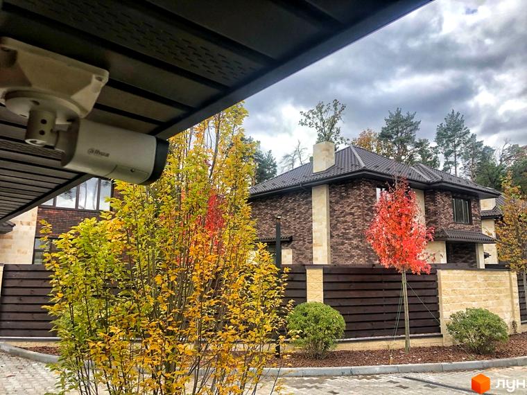 Котеджне містечко Zahrava Village: цегляний будинок з червоними та жовтими деревами на ділянці. Огороджена територія з зеленими кущами та бруківкою.