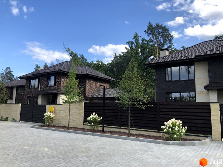Котеджне містечко КМ Zahrava Village. Сучасні двоповерхові будинки з темної цегли та світлими вставками, огороджені дерев'яним парканом, з доглянутою прибудинковою територією та квітучими кущами.