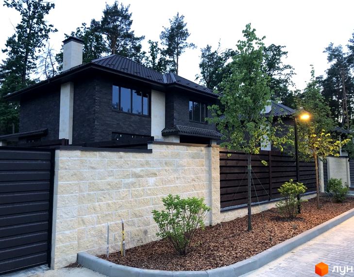 Котеджне містечко KМ Zahrava Village: фасад будинку з темної цегли та світлої плитки, огороджена територія з деревами та ліхтарем.