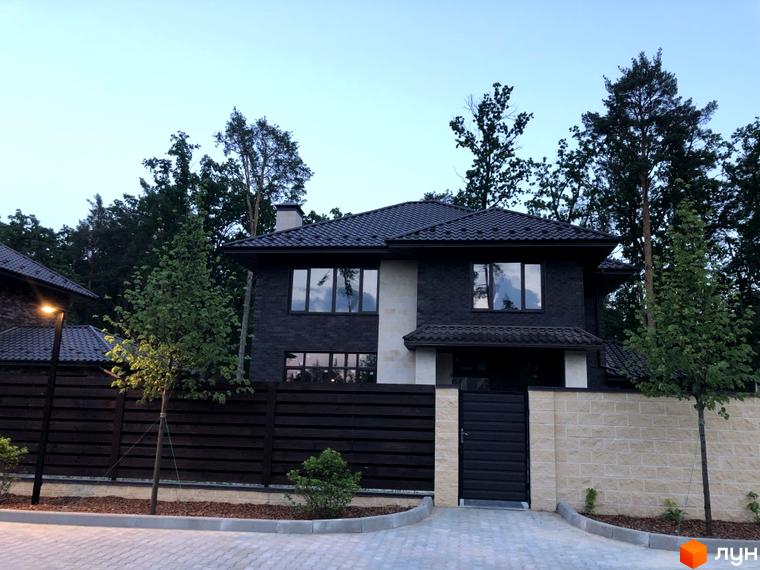 Котеджне містечко Zahrava Village: двоповерховий будинок з темної цегли та світлої плитки, огороджений парканом. Прибудинкова територія з деревами та бруківкою.