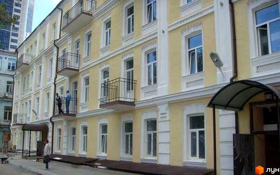 Фасад жовтого житлового комплексу на вулиці Антоновича, 48б, з балконами та вікнами. Поруч видно прибудинкову територію.
