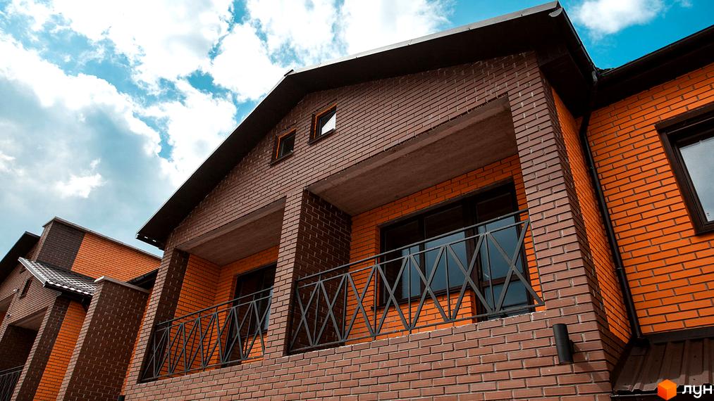 Зовнішній вигляд будинку житлового комплексу КМ Затишне з цегляним фасадом та балконами. Новобудова з цегляним оздобленням та балконами під блакитним небом.