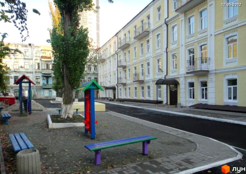 Житловий комплекс на вул. Антоновича, 48б, Київ. Фасад жовтого кольору з білими декоративними елементами. Поруч дитячий майданчик з лавками.