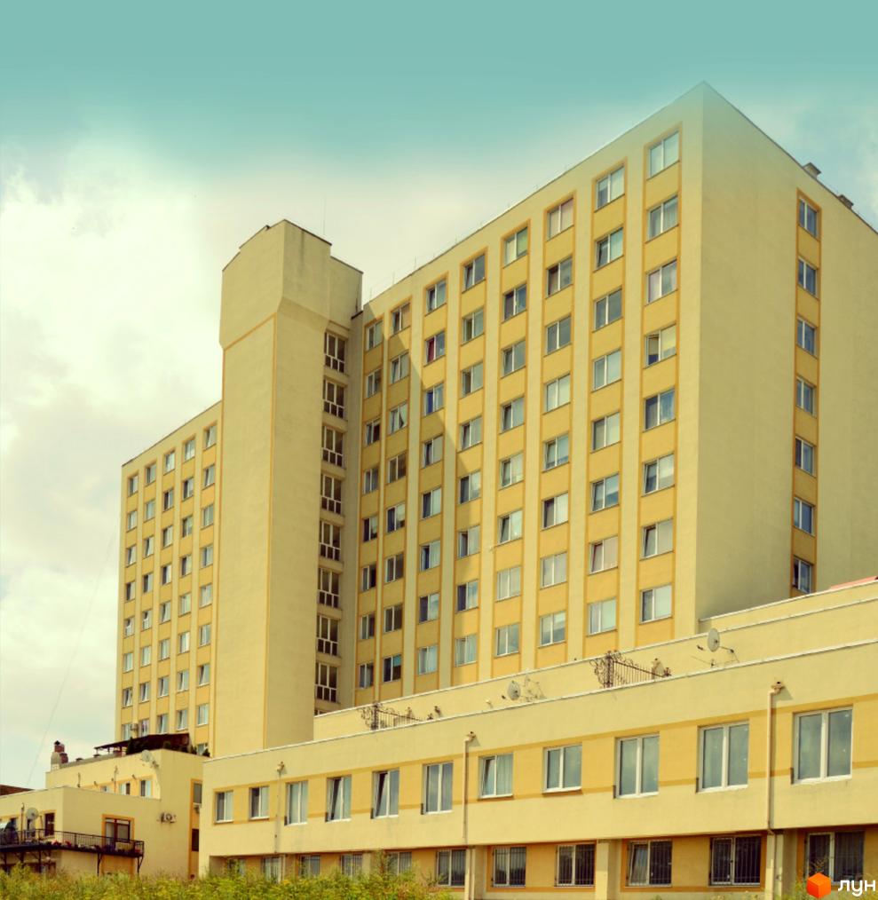 Зовнішній вигляд багатоповерхового житлового комплексу Набережна з жовтим фасадом та численними вікнами. На передньому плані видно нижні поверхи будівель та зелені насадження.