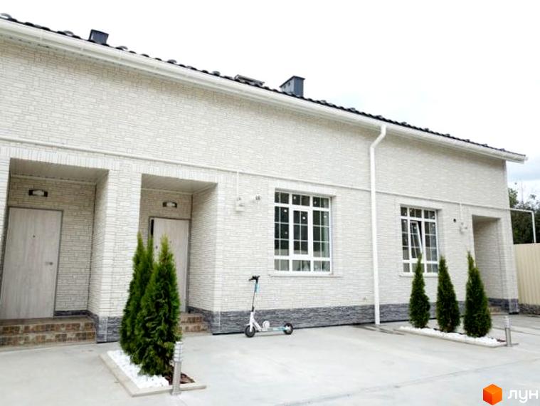 Таунхаус „Грецький“ з білим фасадом та двома входами, перед будинком зелені туї та самокат.