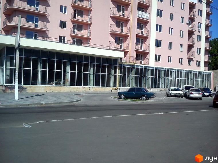 Житловий комплекс Прохорівський з фасадом рожевого кольору та великими вікнами. Прибудинкова територія з парковкою для автомобілів.