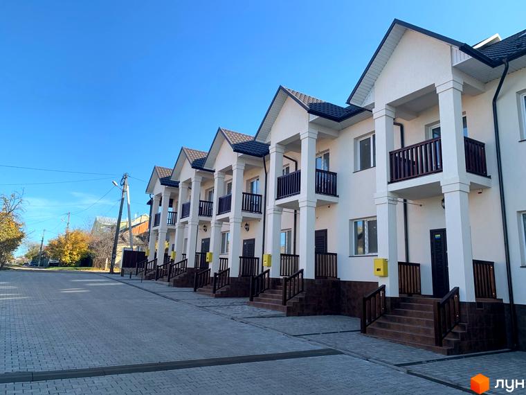 Новобудова на вулиці Обнорського, 10. Фасад будинку з колонами та балконами, вимощена прибудинкова територія.