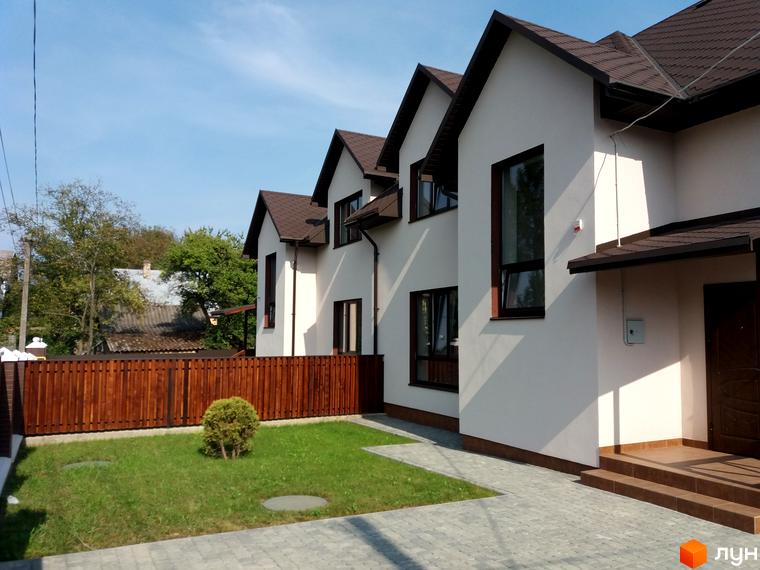 Зовнішній вигляд новобудови з білими стінами та коричневим дахом, огороджена територія з зеленим газоном та дерев'яним парканом.