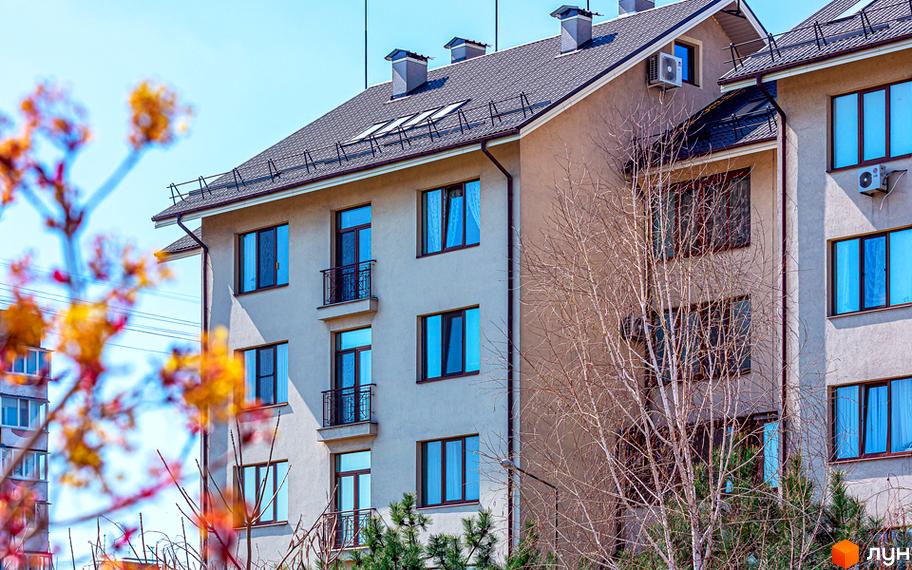 Житловий комплекс Бородино - фасади будівель з вікнами та балконами на тлі блакитного неба. На передньому плані гілки дерев з жовтим листям.