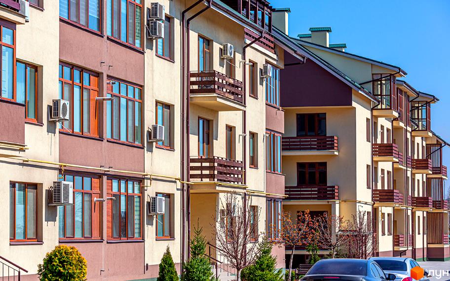 Зовнішній вигляд житлового комплексу ЖК Бородино з балконами та кондиціонерами. На прибудинковій території ростуть дерева та стоять автомобілі.