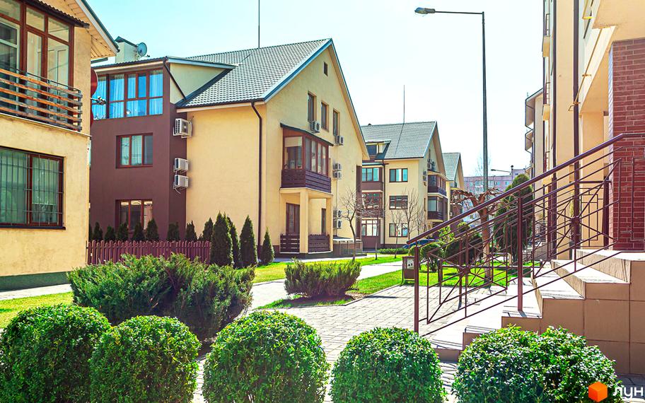 Житловий комплекс Бородино: фасади світло-жовтих та коричневих будинків з балконами, вікнами та кондиціонерами. Прибудинкова територія з доглянутими кущами, деревами та бруківкою.