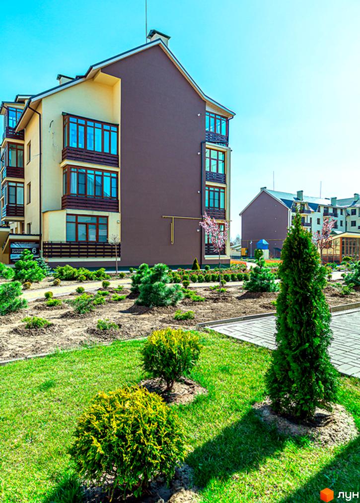 Житловий комплекс Бородино. Зовнішній вигляд будинку з коричневими та бежевими фасадами, великими вікнами та балконами. Прибудинкова територія з зеленими газонами, кущами та деревами.