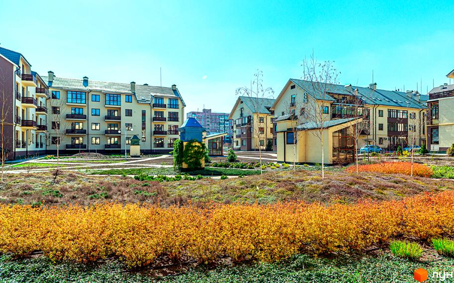 Житловий комплекс Бородино: фасади будинків світло-бежевого кольору з темними вікнами та балконами. Прибудинкова територія з зеленими газонами та кущами з жовтим листям.