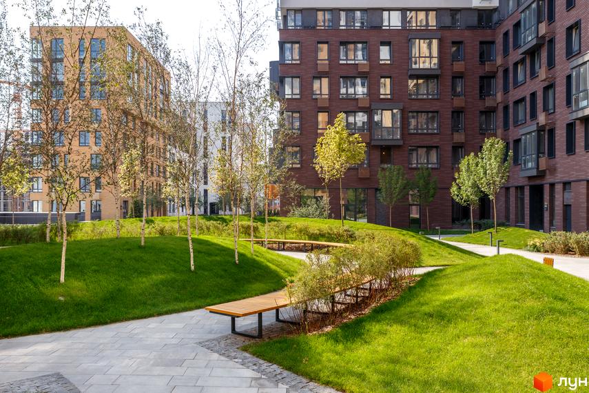 Зображення фасаду та прибудинкової території житлового комплексу Файна Таун. Вигляд на зелену зону з лавками та будівлі з коричневої цегли.