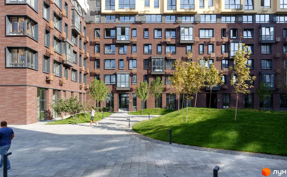 Житловий комплекс Файна Таун: багатоповерховий будинок з коричневим цегляним фасадом, великими вікнами та зеленою прибудинковою територією з деревами.