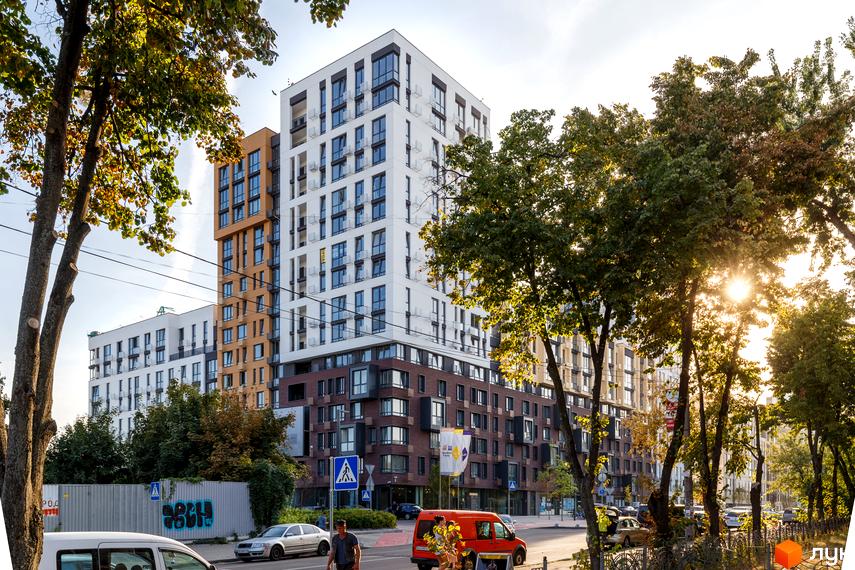 Житловий комплекс Файна Таун: багатоповерховий будинок з біло-коричневим фасадом, розташований вздовж вулиці з деревами та автомобілями.