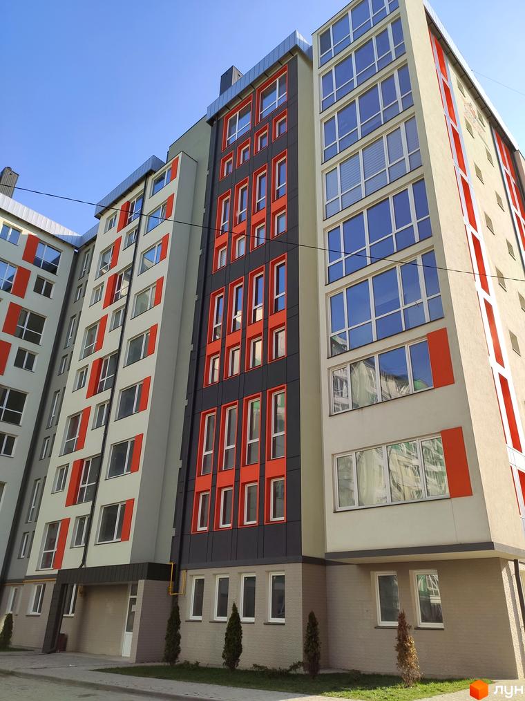 Новобудова на вулиці Руська, 235. Будинок має сіро-бежевий фасад з яскравими помаранчевими елементами та великими вікнами. Біля будинку облаштований зелений двір з деревами.