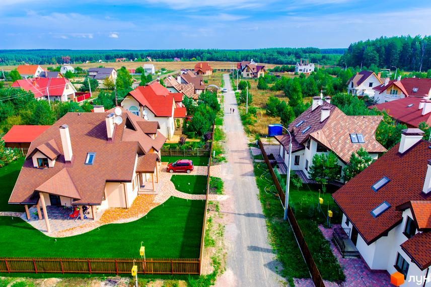 Зображення фасаду будинку в Котеджному містечку Лелечий Хутір. Навколо будинку зелена трава та доріжки.