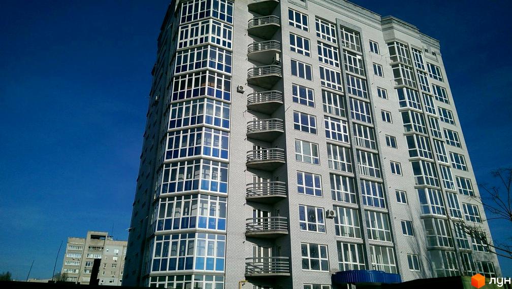 Зовнішній вигляд новобудови по вулиці Гостинна, 77. Багатоповерховий будинок з сірою цегляною облицовкою та великою кількістю скляних балконів.