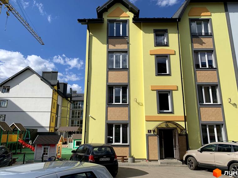 Житловий комплекс Мала Швейцарія: яскрава жовта новобудова з сірими та пісочними елементами фасаду, вікнами та дитячим майданчиком.