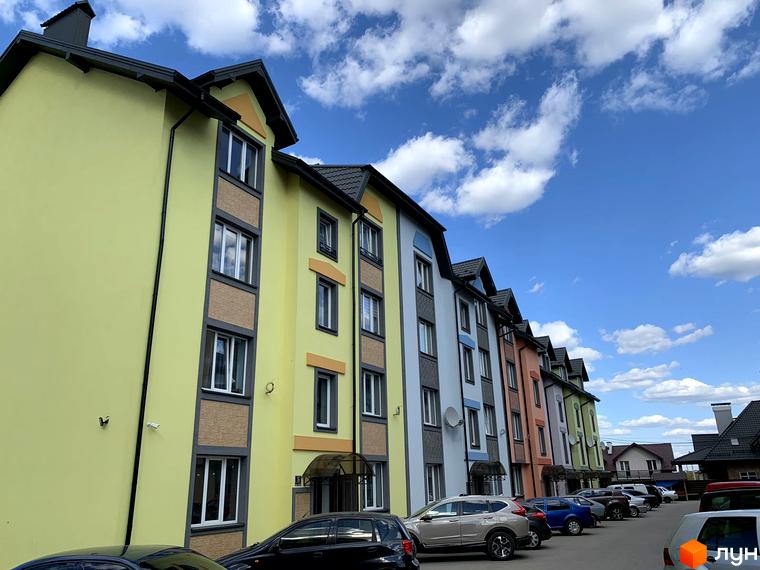 Житловий комплекс Мала Швейцарія: барвисті фасади будинків та парковка перед ними під яскравим небом. Зовнішній вигляд новобудов та прибудинкова територія.