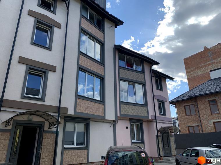 Зовнішній вигляд новобудови ЖК Мала Швейцарія з вікнами та фасадом. На прибудинковій території видно автомобілі та паркан.