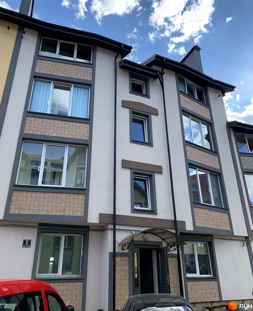 Зовнішній вигляд житлового комплексу Мала Швейцарія з великими вікнами та сірим фасадом. Навколо будинку видно елементи прибудинкової території.