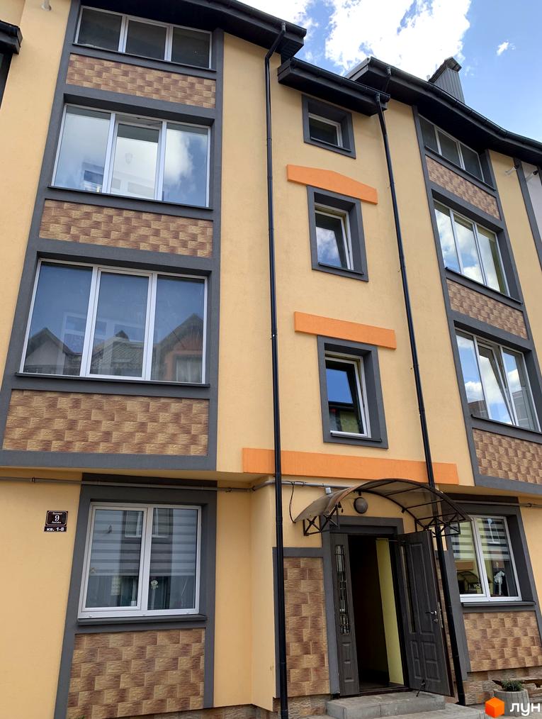 Фасад житлового комплексу Мала Швейцарія з вікнами та вхідною групою. Зовнішній вигляд новобудови з жовтою штукатуркою та декоративними елементами.