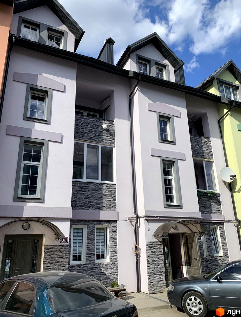 Фасад новобудови ЖК Мала Швейцарія з сірим оздобленням та вікнами. Прибудинкова територія з автомобілями та навісом над входом.