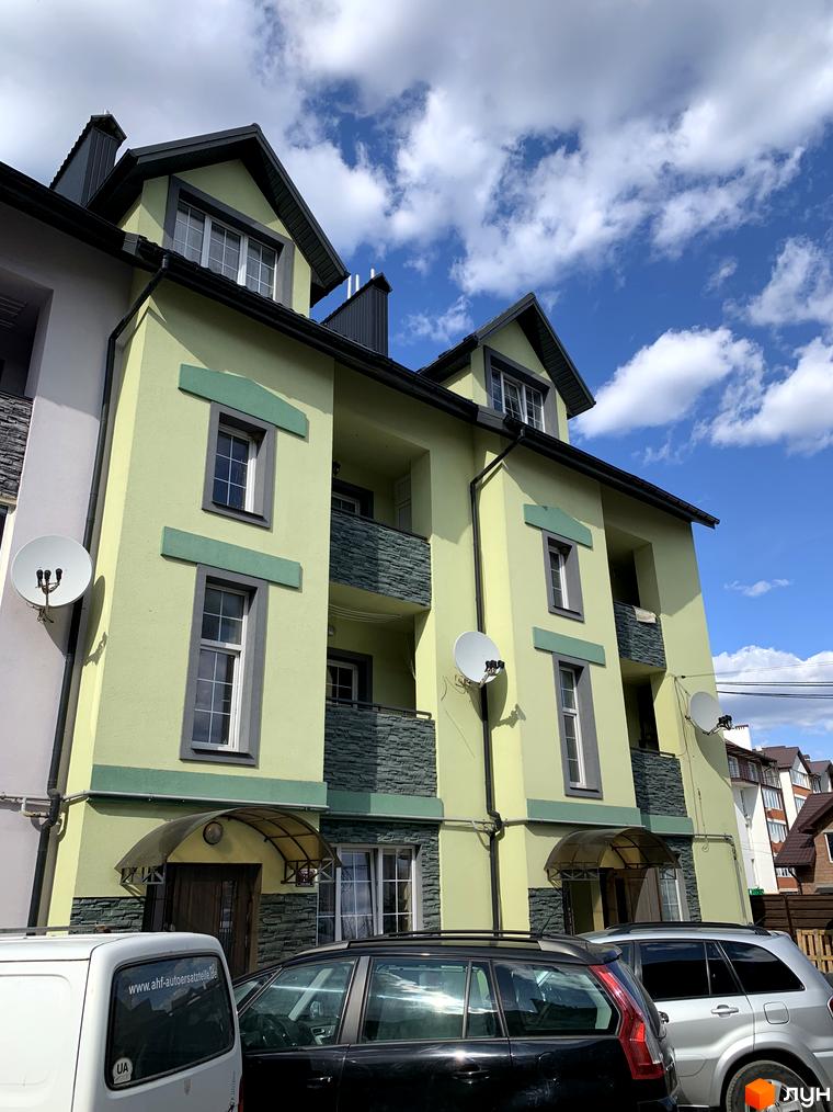 Зовнішній вигляд світло-зеленої новобудови ЖК Мала Швейцарія з сірими елементами та балконами. Навколо будинку розташовані автомобілі та супутникові антени.