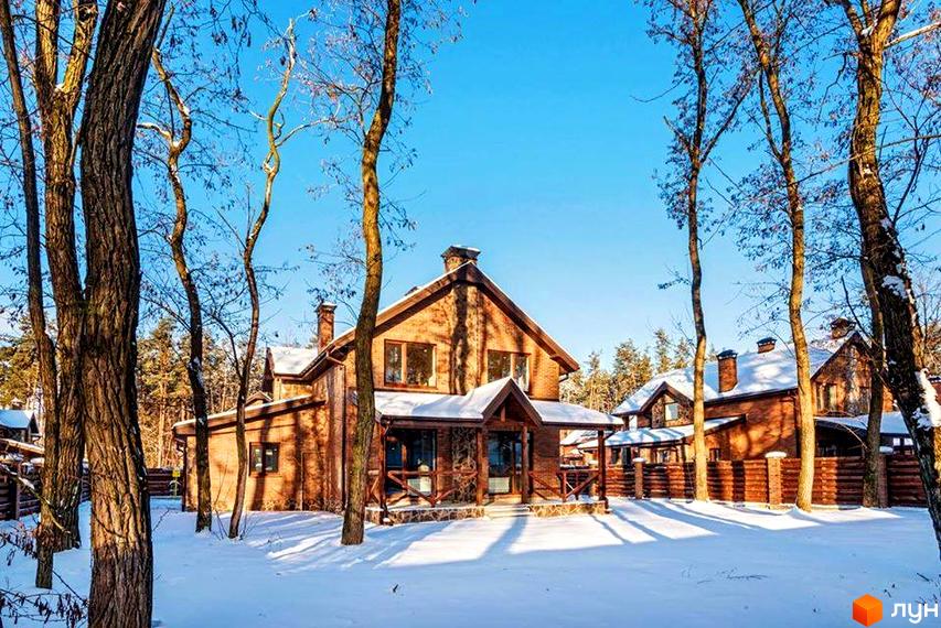 Котеджне містечко КМ Парк хаус у зимовому лісі. Цегляні будинки з дерев'яними елементами під снігом, огороджені парканом.