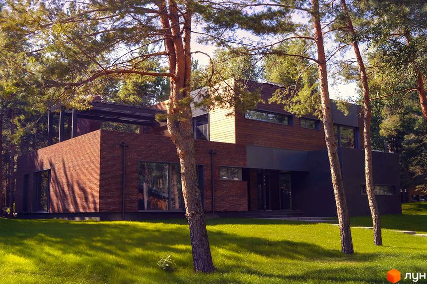 Зображення будинку в Котеджному містечку Goodlife Park. Двоповерхова будівля з цегляним фасадом та великими вікнами, зелений газон.