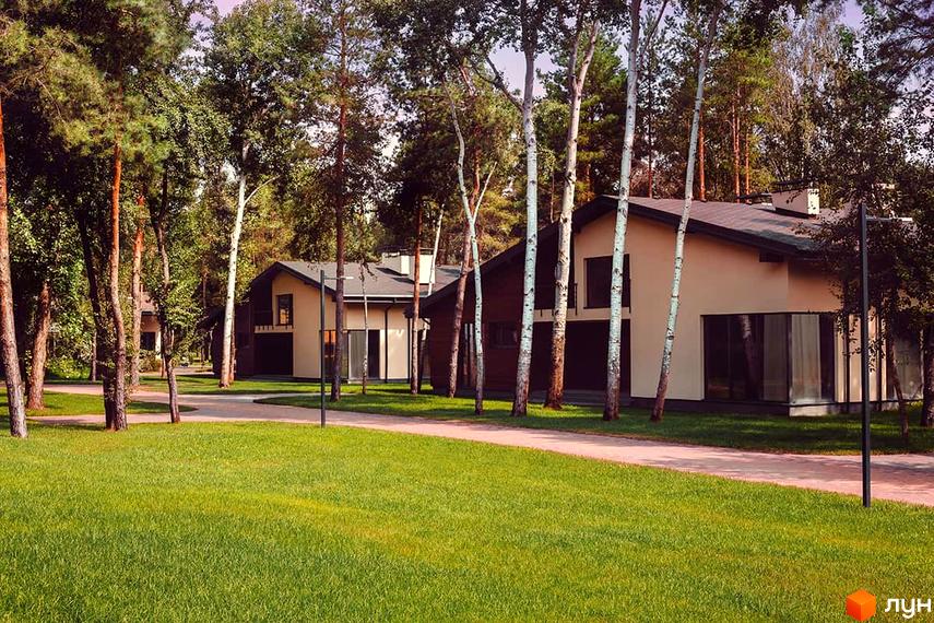 Зображення будинків у Котеджному містечку Goodlife Park. Двоповерхові будівлі з великими вікнами, оточені деревами та зеленим газоном.