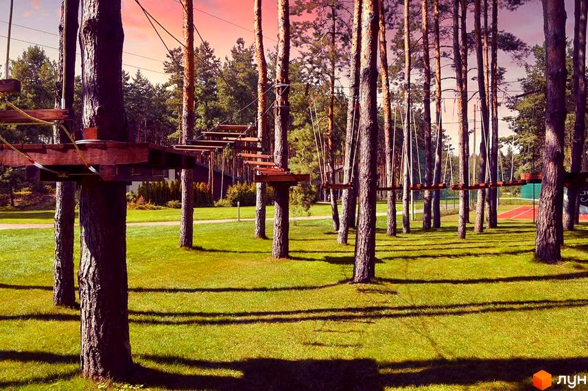 Котеджне містечко Goodlife Park з мотузковим парком на території. Дерева та зелений газон навколо котеджів.
