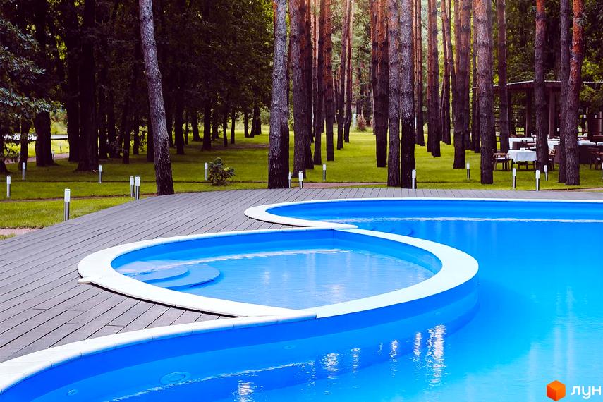Басейн на території Котеджного містечка Goodlife Park. Навколо басейну дерев'яний настил та сосновий ліс.