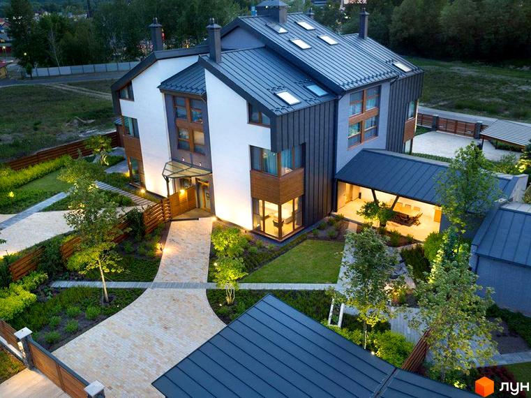 Зовнішній вигляд будинку в КМ. Будинок має темну покрівлю та світлий фасад. На прибудинковій території є доріжки, газон та дерева.