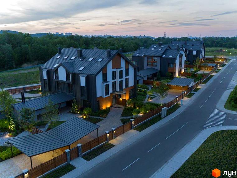 Зображення фасаду та прибудинкової території QDRO - котеджі з темною покрівлею та світлими стінами. На території розташовані доріжки, зелені насадження та вуличне освітлення.