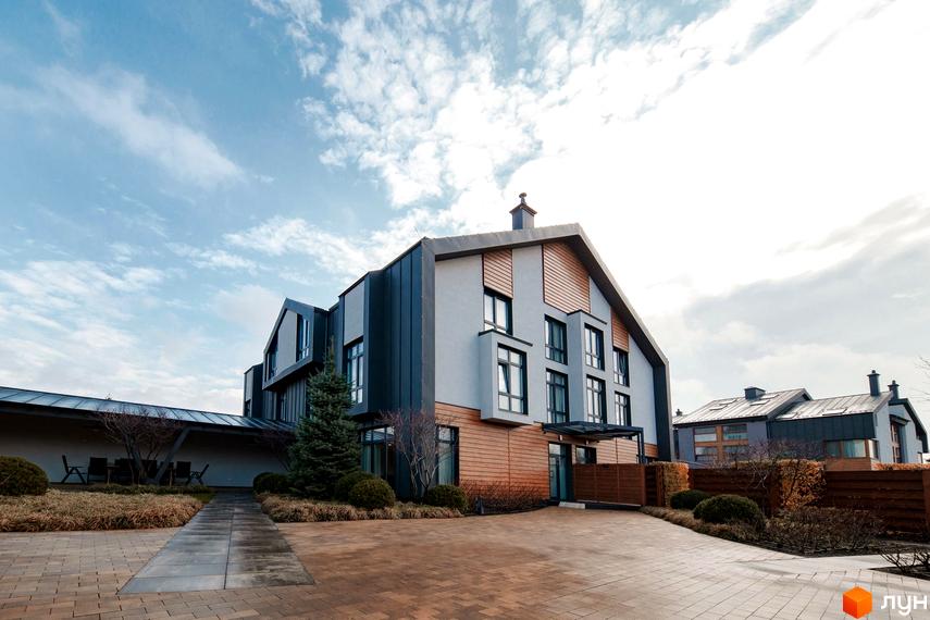 Зображення фасаду будинку в стилі таунхаус. На передньому плані бруківка та зелені насадження.