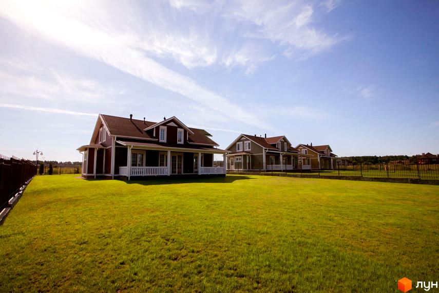 Будинки з коричневою покрівлею та білими верандами на тлі блакитного неба. Зелена галявина перед будинками.