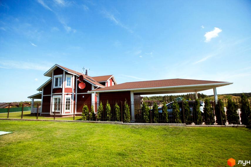 Двоповерховий будинок з коричневим дахом та білими вікнами. На передньому плані зелена галявина з доглянутим газоном.